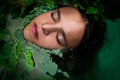 Portrait of a young woman laying in water with a garland of leaves . concept of Ophelia or mermaid. top view portrait