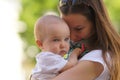 Portrait of young woman with long hair in white t-shirt hugging little baby in white clothes, closeup, green background