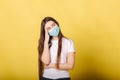 Portrait of young woman in medical mask stand in frond of yellow background. Girl has a headache from the face mask Royalty Free Stock Photo