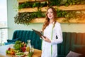 Portrait of a young woman nutritionist in medical gown standing with clipboard and tape measure in the office with healthy food on Royalty Free Stock Photo