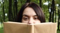 Portrait of a young woman with an open untitled book held close to her face. Brunette covering half of her face with a book in the Royalty Free Stock Photo