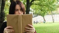 Portrait of a young woman with an open untitled book held close to her face. Brunette covering half of her face with a book in the Royalty Free Stock Photo