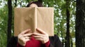 Portrait of a young woman with an open untitled book held close to her face. Brunette covering her face with a book in the park on Royalty Free Stock Photo