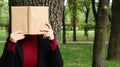 Portrait of a young woman with an open untitled book held close to her face. Brunette covering her face with a book in the park on Royalty Free Stock Photo