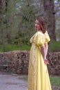 Young woman outdoors in historical yellow dress holding cup