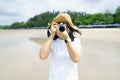 Portrait young woman photography wearing a hat using her mirrorless camera covering her face on the beach and smiling. photography Royalty Free Stock Photo
