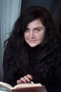 Portrait of young woman plus size with wealth of brown hair, she is reading a book next to the window