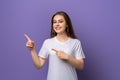 Portrait of young woman pointing fingers aside and looking with positive face expression, standing over purple background Royalty Free Stock Photo