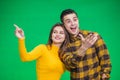 Portrait of young woman pointing at something ahead isolated on green background, her boyfriend is looking at something Royalty Free Stock Photo