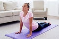 Portrait of young woman practicing yoga at home indoor, copy space. Girl practicing cobra pose, full length. Royalty Free Stock Photo