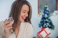 Portrait of a young woman during preparations for Christmas at home. Toothy smiling woman with red lips holding gift box and vine Royalty Free Stock Photo