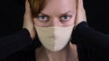 Portrait of a young woman in a protective mask covers her ears on a black background, the concept of unwillingness to listen, hear Royalty Free Stock Photo