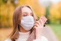 Portrait young woman in protective mask playing ukulele guitar in autumn park, healthy travel