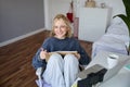 Portrait of young woman reading her notes on journal, sitting at home on chair, smiling and looking happy, doing Royalty Free Stock Photo