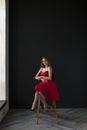 Portrait of a young woman in a red dress sitting on a high bar stool Royalty Free Stock Photo