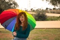 Portrait of young woman, red hair, freckles, with a rainbow umbrella, happy, in an outdoor park. Concept color, happiness, well-