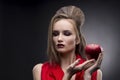 Portrait of the young woman in a red scarf with a vanguard hairstyle which holds in hand red apple on a gray background Royalty Free Stock Photo