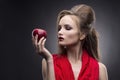 Portrait of the young woman in a red scarf with a vanguard hairstyle which holds in hand red apple on a gray background Royalty Free Stock Photo