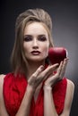 Portrait of the young woman in a red scarf with a vanguard hairstyle which holds in hand red apple on a gray background Royalty Free Stock Photo