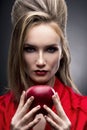 Portrait of the young woman in a red scarf with a vanguard hairstyle which holds in hand red apple on a gray background