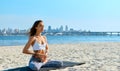 Portrait of young woman relaxing practicing yoga and meditation on the sand beach with city background. Sporty girl is Royalty Free Stock Photo