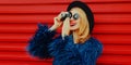 Portrait of young woman with retro camera taking picture wearing blue faux fur coat, round hat