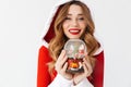 Portrait of young woman 20s wearing Santa Claus red costume smiling and holding Christmas snow ball, isolated over white Royalty Free Stock Photo