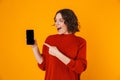 Portrait of young woman holding and demonstrating smartphone while standing isolated over yellow background Royalty Free Stock Photo