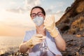 Portrait of young woman scientist-ecologist wearing eyeglasses, mask and rubber gloves tests flask of water. Concept of