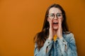 Portrait of young woman screams with excitement, keeps hands near mouth, wears denim jacket and eyeglasses Royalty Free Stock Photo