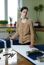 Portrait of a young woman seamstress in a home Studio. Looks appraisingly at client. Holding a pair of scissors. Handmade concept