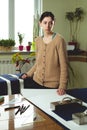 Portrait of a young woman seamstress in a home Studio. Looks appraisingly at client. Holding a pair of scissors. Handmade concept