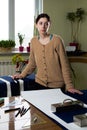 Portrait of a young woman seamstress in a home Studio. Looks appraisingly at client. Holding a pair of scissors. Handmade concept