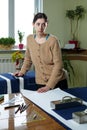 Portrait of a young woman seamstress in a home Studio. Looks appraisingly at client. Holding a pair of scissors. Handmade concept