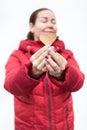 Portrait of young woman with shape of heart in hands narrowing eyes with pleasure, red winter jacket, white background