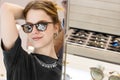 Portrait of a young woman shopping, standing in store and trying sunglasses near a mirror Royalty Free Stock Photo