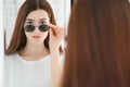 Portrait of a young woman shopping, standing in store and trying sunglasses near a mirror. Royalty Free Stock Photo