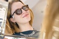 Portrait of a young woman shopping, standing in store and trying sunglasses near a mirror Royalty Free Stock Photo