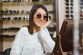 Portrait of a young woman shopping, standing in store and trying sunglasses near a mirror Royalty Free Stock Photo