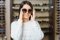 Portrait of a young woman shopping, standing in store and trying sunglasses near a mirror Royalty Free Stock Photo