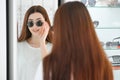 Portrait of a young woman shopping, standing in store and trying sunglasses near a mirror. Royalty Free Stock Photo