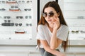 Portrait of a young woman shopping, standing in store and trying sunglasses near a mirror. Royalty Free Stock Photo