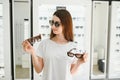 Portrait of a young woman shopping, standing in store and trying sunglasses near a mirror. Royalty Free Stock Photo