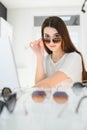 Portrait of a young woman shopping, standing in store and trying sunglasses near a mirror. Royalty Free Stock Photo