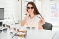 Portrait of a young woman shopping, standing in store and trying sunglasses near a mirror. Royalty Free Stock Photo