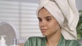 Portrait of a young woman after a shower in front of a mirror wearing a bath towel on her head close up. Woman examines Royalty Free Stock Photo