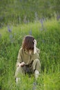 Portrait of a young woman sitting in a field on the spring grass among purple flowers. stylish girl enjoys Sunny spring Royalty Free Stock Photo