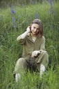 Portrait of a young woman sitting in a field on the spring grass among purple flowers. stylish girl enjoys Sunny spring Royalty Free Stock Photo