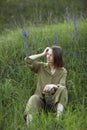 Portrait of a young woman sitting in a field on the spring grass among purple flowers. stylish girl enjoys Sunny spring weather. Royalty Free Stock Photo