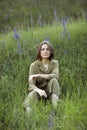 Portrait of a young woman sitting in a field on the spring grass among purple flowers. stylish girl enjoys Sunny spring Royalty Free Stock Photo